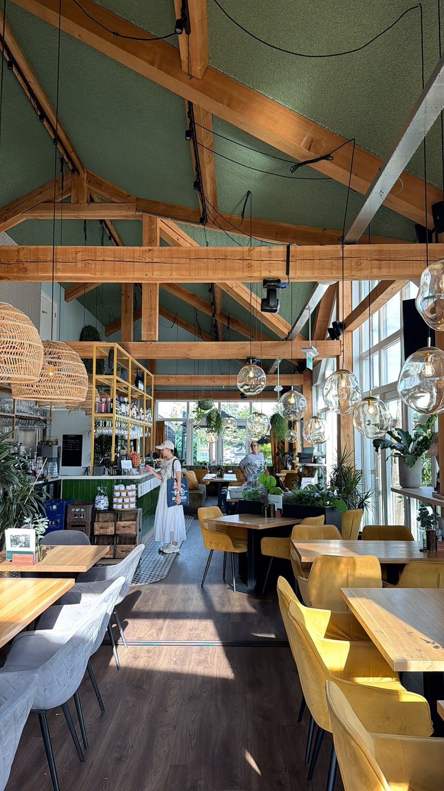 Het interieur van De Eetkamer met houten spanten, groene wanden en rieten lampen